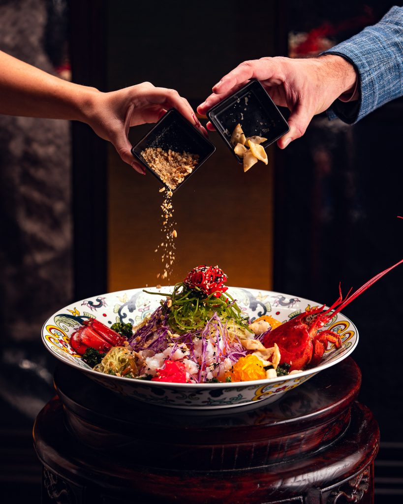 people sprinkling toppings onto a dish 